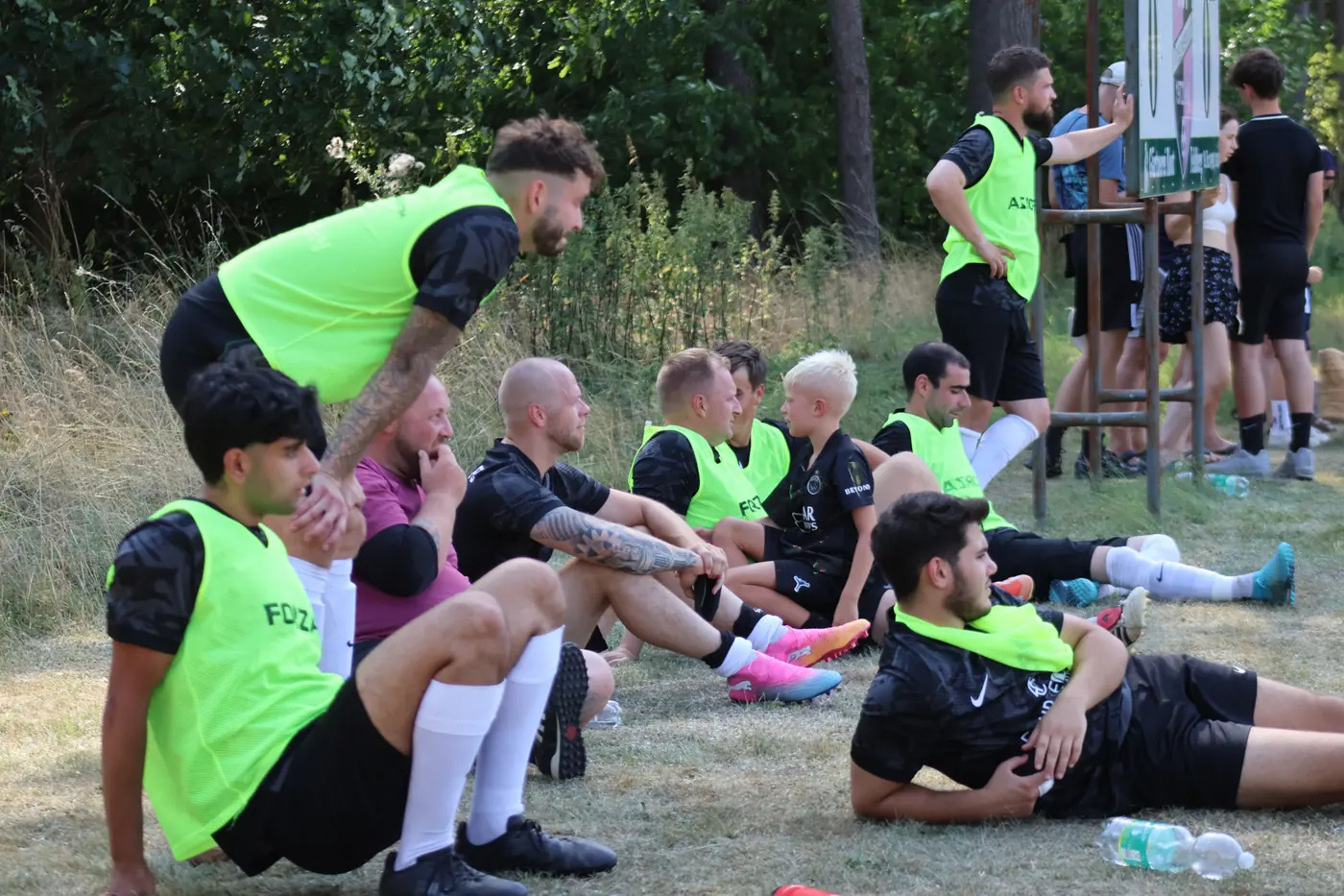 Auswechselspieler sitzen in Leibchen am Spielfeldrand im Gras